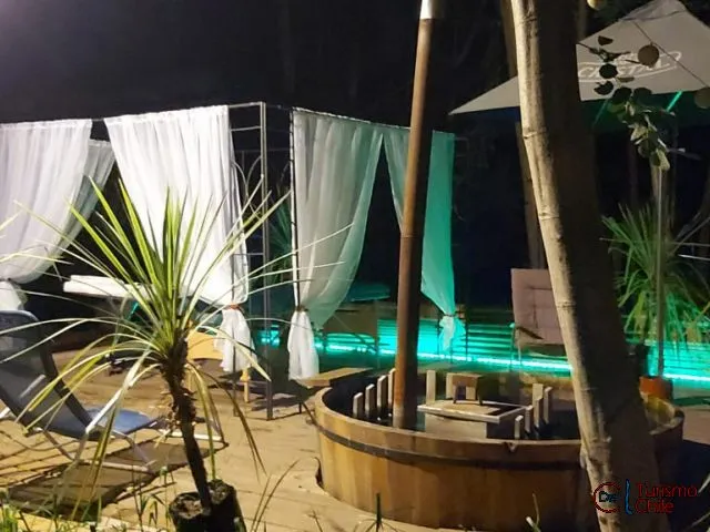 Piscina iluminada de noche con reposeras blancas en Cabañas Rucalhue