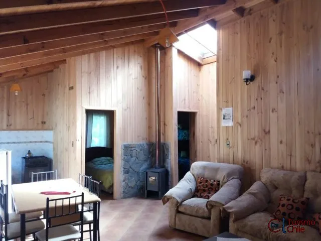 Living con living-comedor, salamandra y vigas de madera a la vista en cabaña Rucalhue