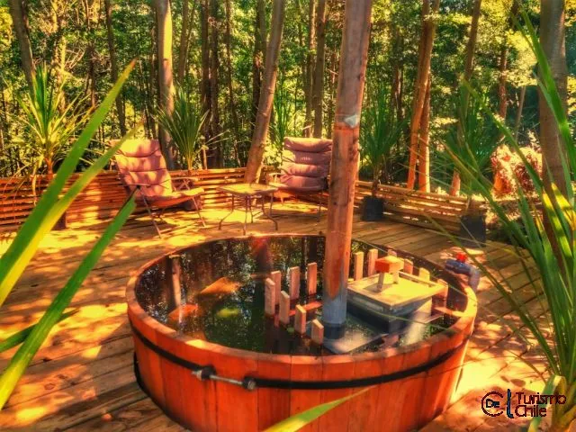 Tina de agua caliente en deck de madera rodeada de bosque nativo en Cabañas Rucalhue
